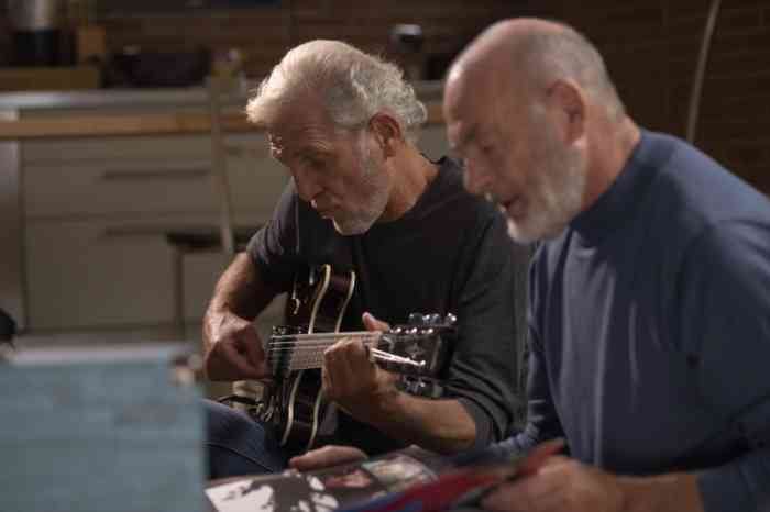 Two senior men singing and playing guitar