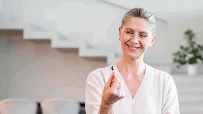 A woman sitting on the sofa holding a hearing aid in her right hand