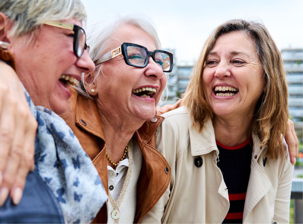 Trois femmes âgées rient joyeusement en plein air, partageant un moment de complicité.