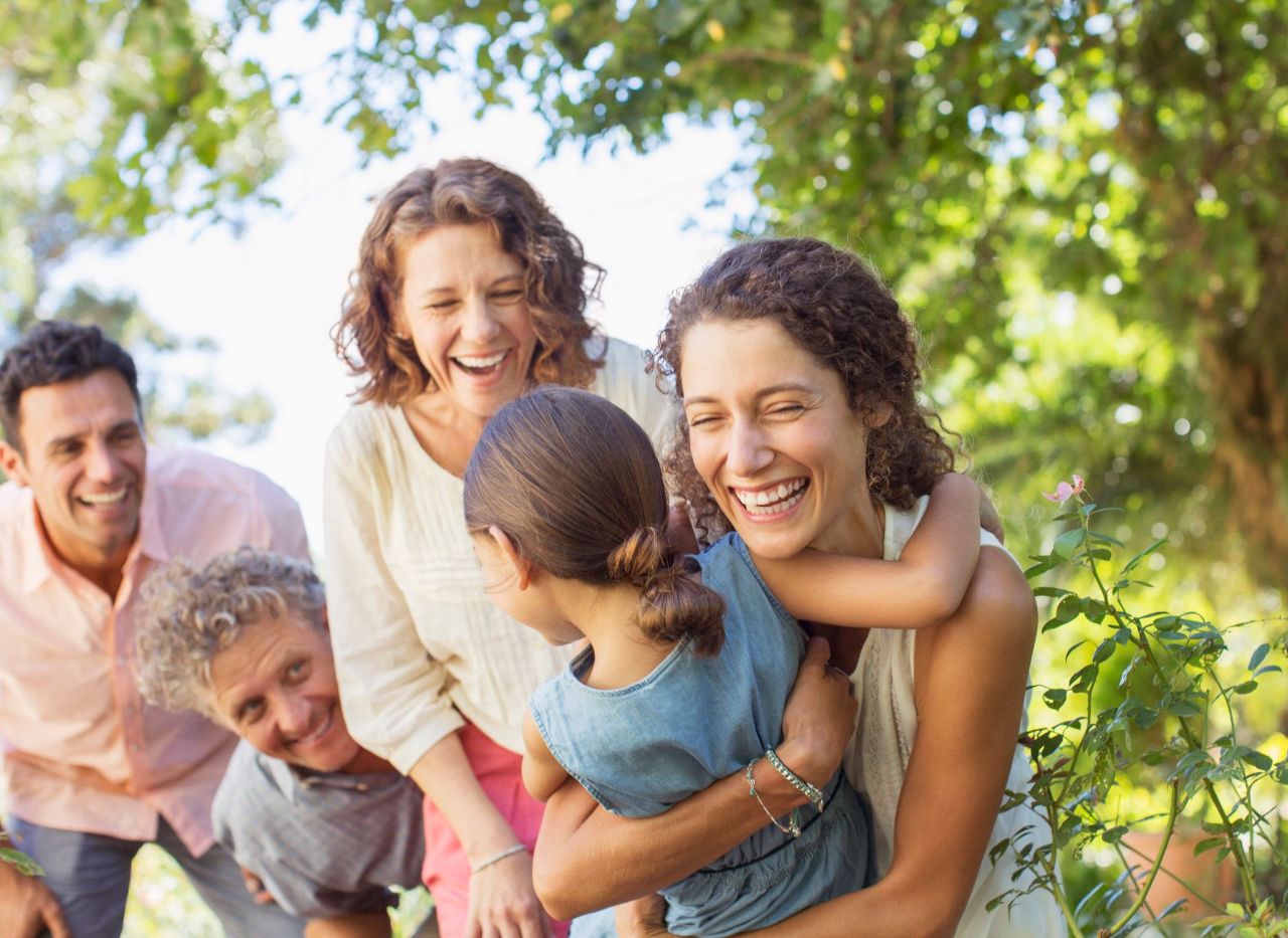 Une famille souriante joue et profite d’un moment en plein air sous les arbres.