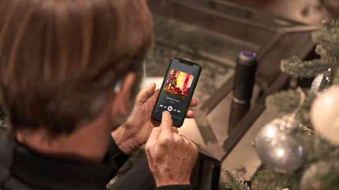 Homme vu de dos portant un appareil auditif en train d'écouter de la musique avec son smartphone.