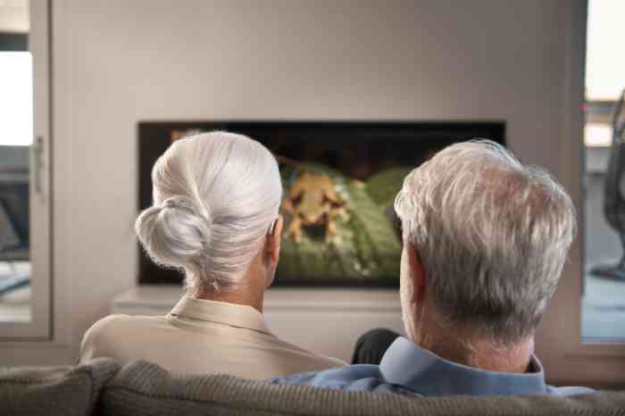Personnes âgées vues de dos en train de regarder la télévision, la femme porte un appareil auditif.