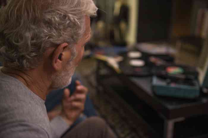 A senior man with in-the-ear hearing aids playing air guitar