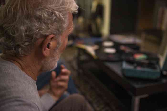 Grandfather in profile with hearing aids pretending to play an invisible guitar.