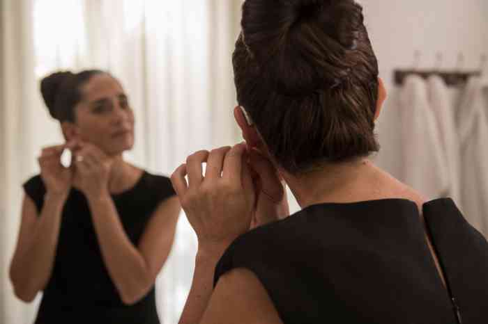 Woman with invisible hearing aids in her bathroom smiling at the mirror