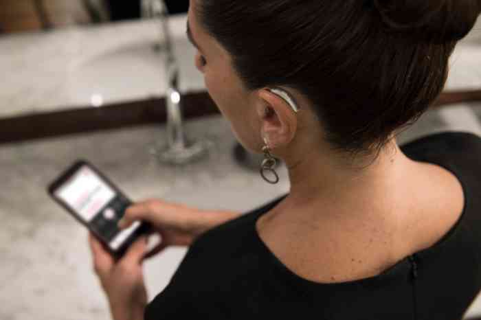 Young girl wearing Behind-The-Ear hearing aid looking at her smartphone