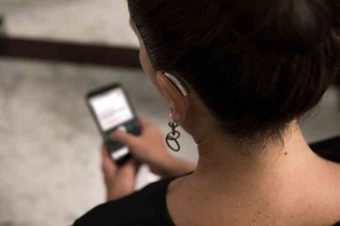 Femme portant une prothèse auditive à l'oreille gauche en train de consulter son smartphone.
