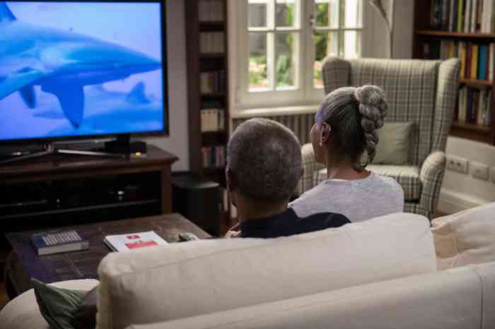 A senior couple with Behind-The-Ear hearing aids watching TV 