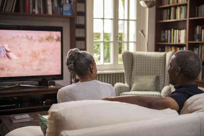 Senior couple with hearing aids watching TV on their sofa 