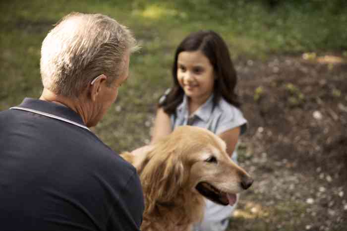 Homme senior vu de dos portant un appareil auditif à l'oreille droite parlant avec sa petite-fille et son chien.