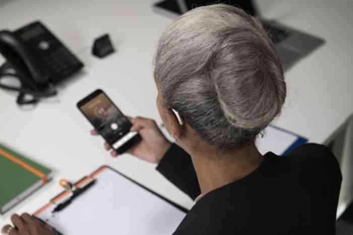 A business woman checks her hearing aid's app via smartphone