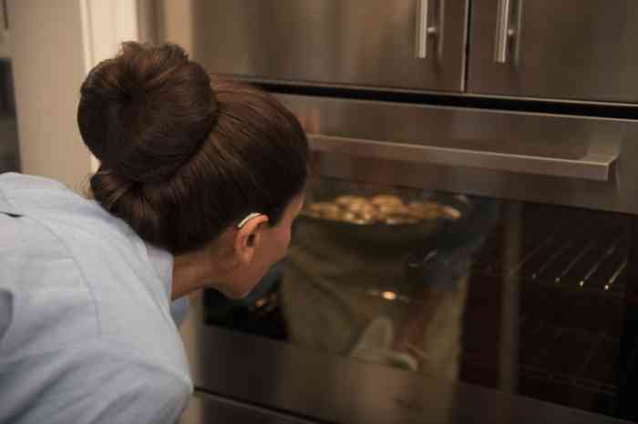 A woman wearing a BTE hearing aid is baking a dish