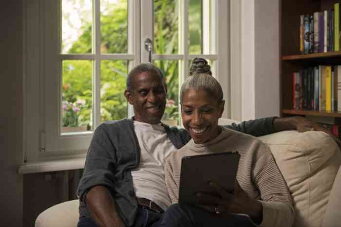 A couple sitting on a sofa, smiling to their tablet