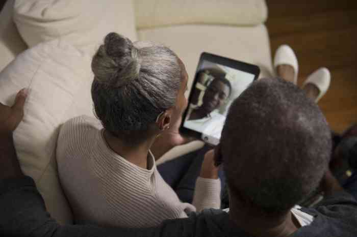 Un couple assis dans un canapé en train de converser avec leur fils sur une tablette.