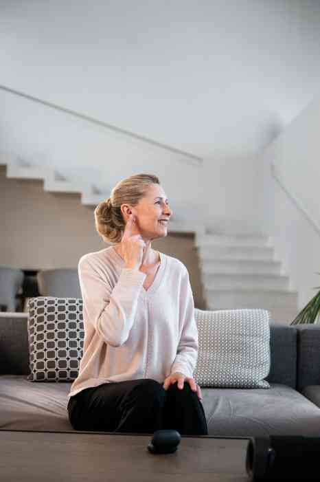 A woman sitting on the sofa, happily wearing her hearing aid.