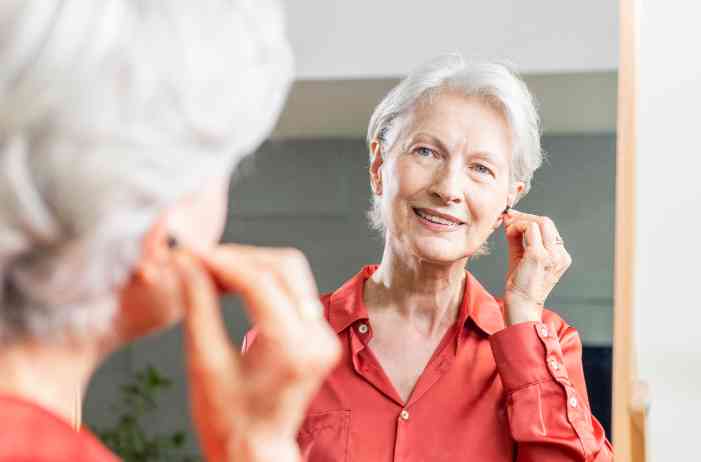 A woman looking at herself in the mirror while wearing a hearing aid.
