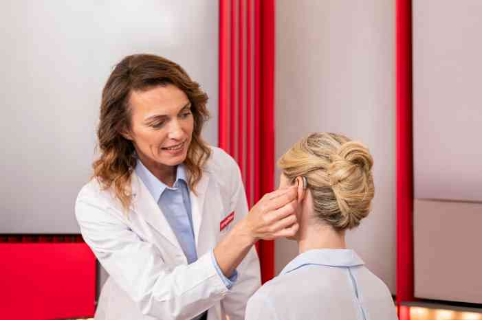 An audiologist fitting a hearing aid into a patient's ear