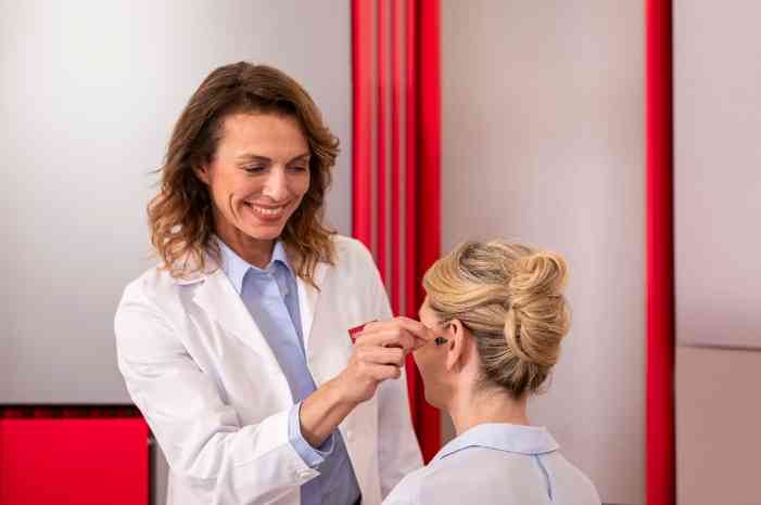 A female audiologist fitting a hearing aid on a patient.