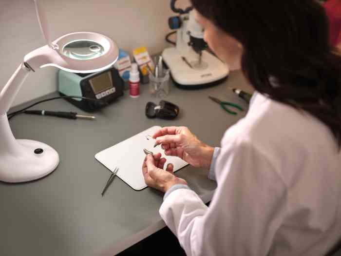 audiologist in a laboratory working on a hearing aid, wearing a coat.
