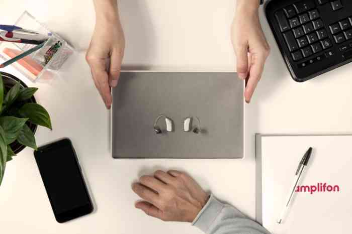 Deux aides auditives sur un plateau gris, mains les présentant.