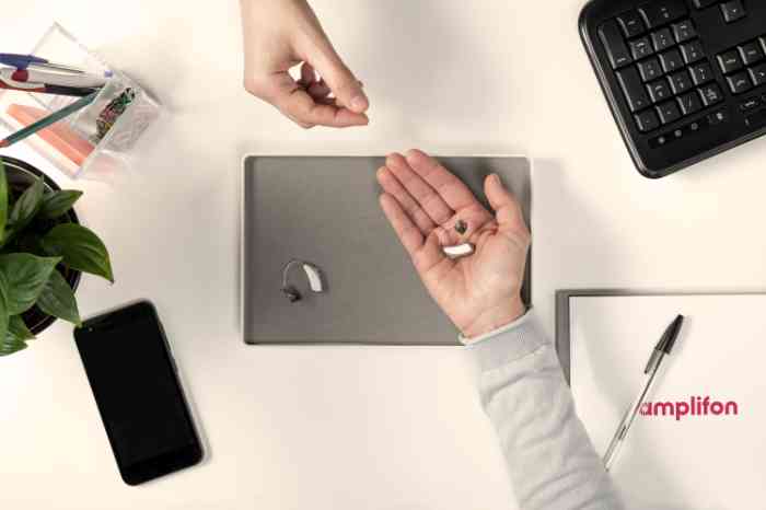 Hand holding a hearing aid above a gray tray.