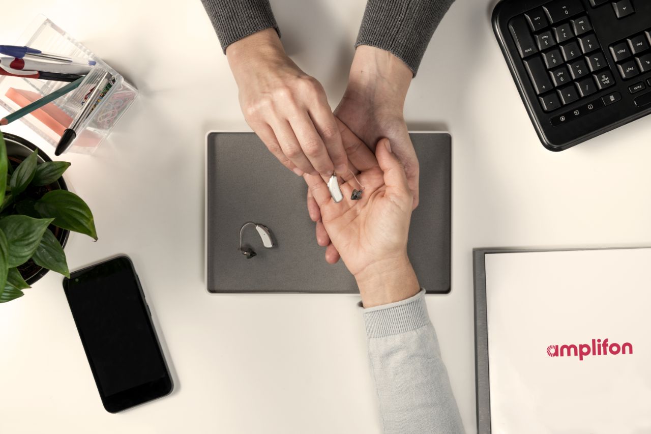 Audiologist placing a hearing aid on patient's hand.