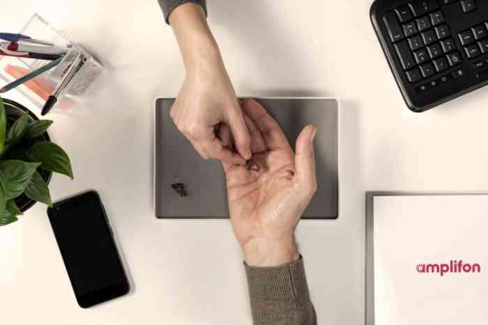 Audiologe übergibt ein Hörgerät in die Hand eines Patienten.