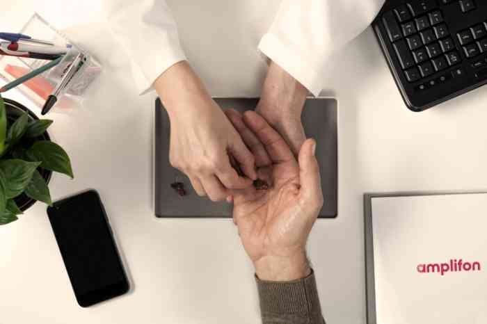 Audiologiste plaçant une aide auditive sur la main du patient.