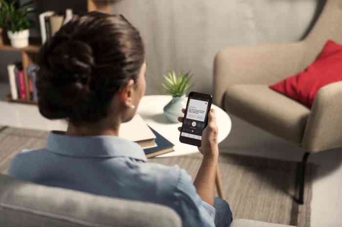 Femme utilisant une application sur un smartphone, assise sur un canapé dans un salon.