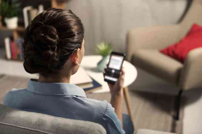 Femme vue de dos portant un appareil auditif et consultant l'application Amplifon sur son smartphone.
