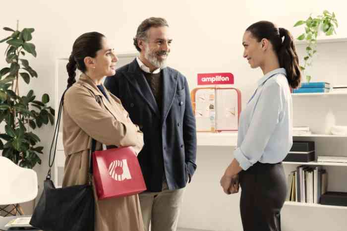 Audiologiste en chemise bleue discutant avec un couple souriant en magasin Amplifon.
