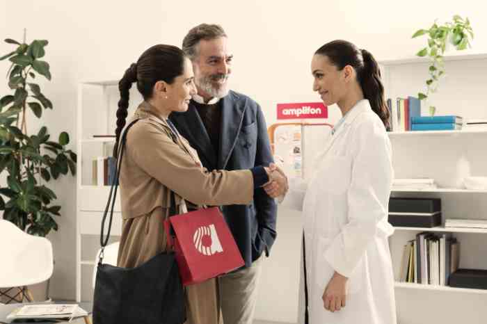 Audiologist in lab coat shaking hands with a smiling couple in an Amplifon store.