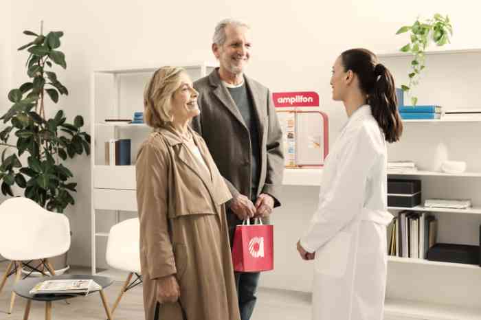 Audiologist in lab coat talking with a happy elderly couple in an Amplifon store.