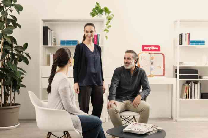 Audiologist standing and talking with two seated clients in an Amplifon store.