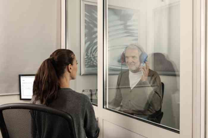 Une audioprothésiste Amplifon fait passer un test auditif à une cliente, assise dans une cabine et portant un casque.