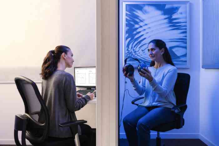 An audiologist without a lab coat is about to conduct a hearing test on a woman