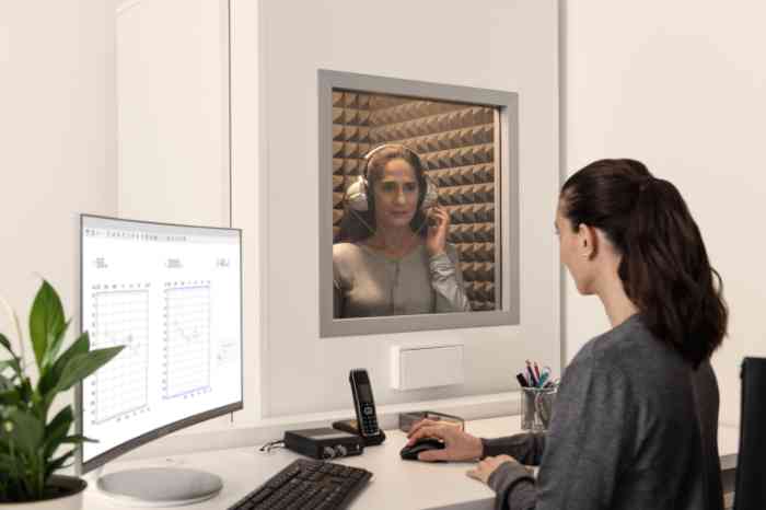 Une audioprothésiste Amplifon fait passer un test auditif à un client, assise dans une cabine et portant un casque.
