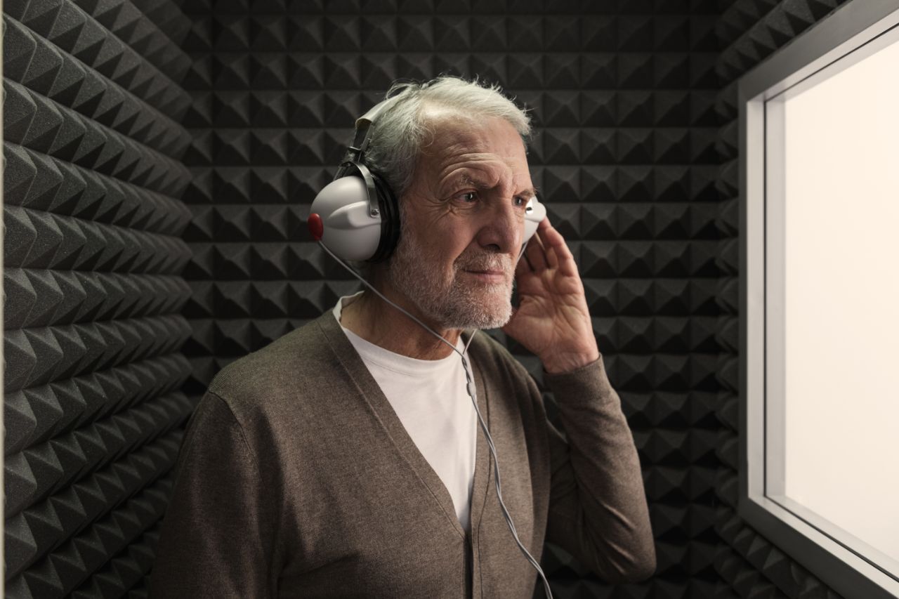 Un uomo in cabina audiometrica con una mano appoggiata sulle cuffie