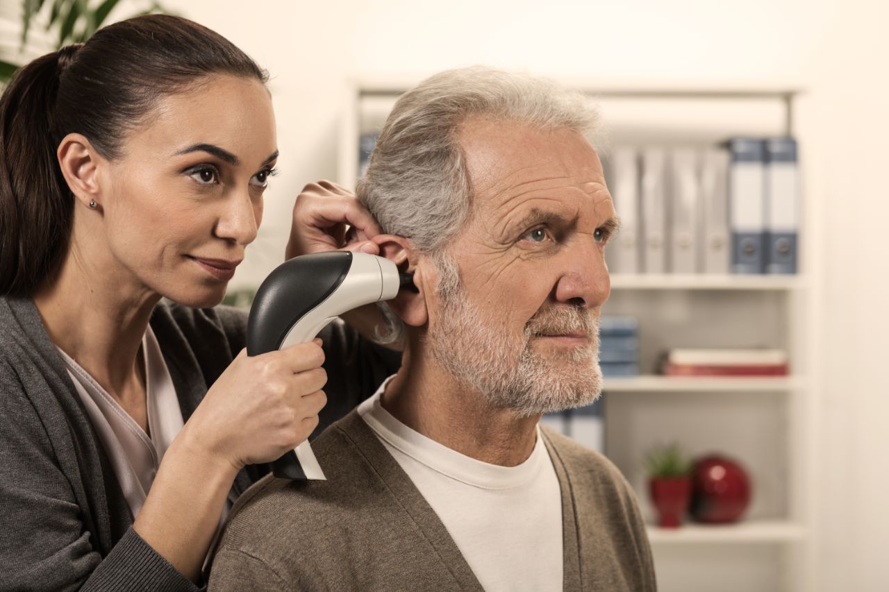 Un audiologiste sans blouse examine l'oreille d'un homme âgé avec un vidéo otoscope.