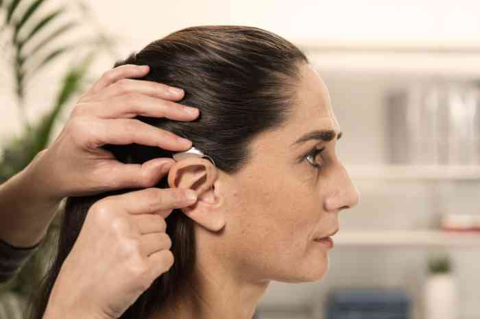 Audioprothésiste plaçant un appareil auditif contour d'oreille sur l'oreille droite d'une cliente.