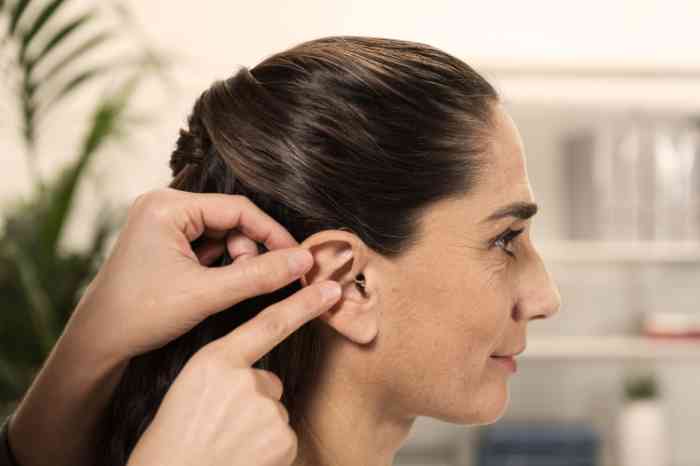 Audioprothésiste plaçant un appareil auditif intra-auriculaire dans l'oreille droite d'une cliente.