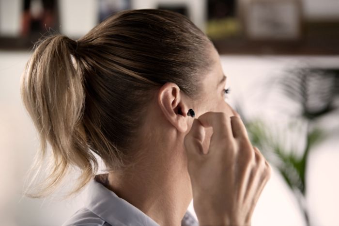 Une jeune femme de profil place un appareil auditif ITE dans son oreille