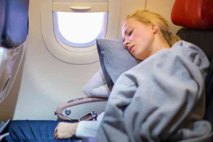 Femme endormie à bord d'un avion, le côté droit de sa tête reposant sur un coussin. 