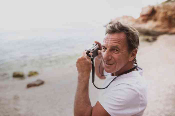 Homme senior au bord de la mer en train de prendre une photo.