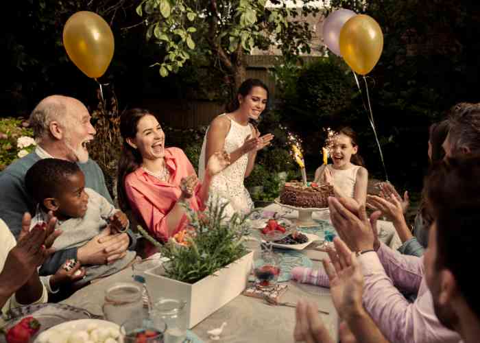 Famille réunie autour d'une table en extérieur fêtant l'anniversaire d'une petite fille.