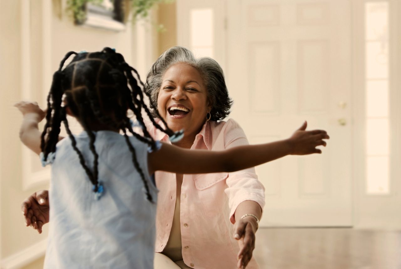 Grand-mère souriante accueillant sa petite-fille les bras ouverts.