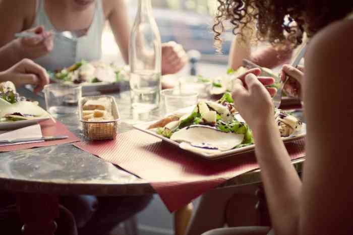 Gros plan sur une table de restaurant en extérieur, où des amis sont en train de manger leur salade.