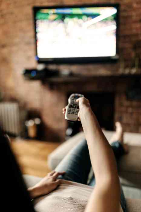 Personne assise dans un canapé en train de regarder la télévision et pointant l'écran avec une télécommande.
