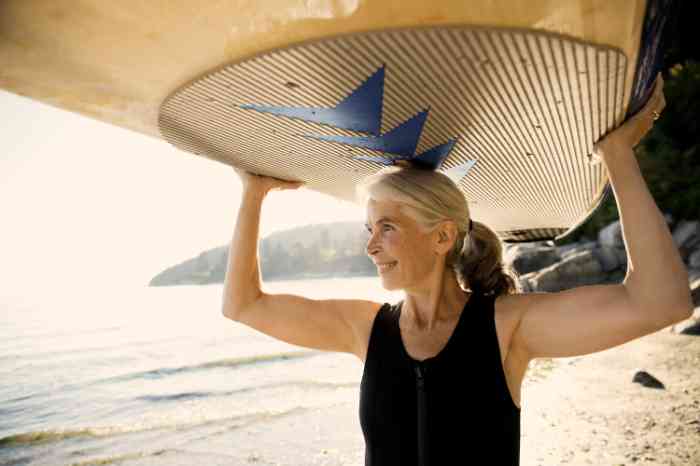 A senior woman with her surfboard on the beach