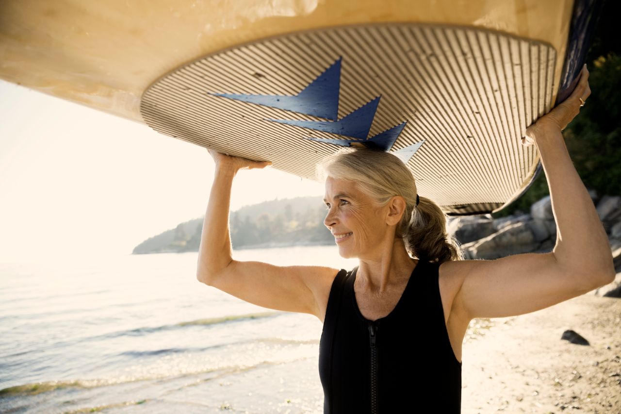 Femme à la plage soulevant une planche de surf